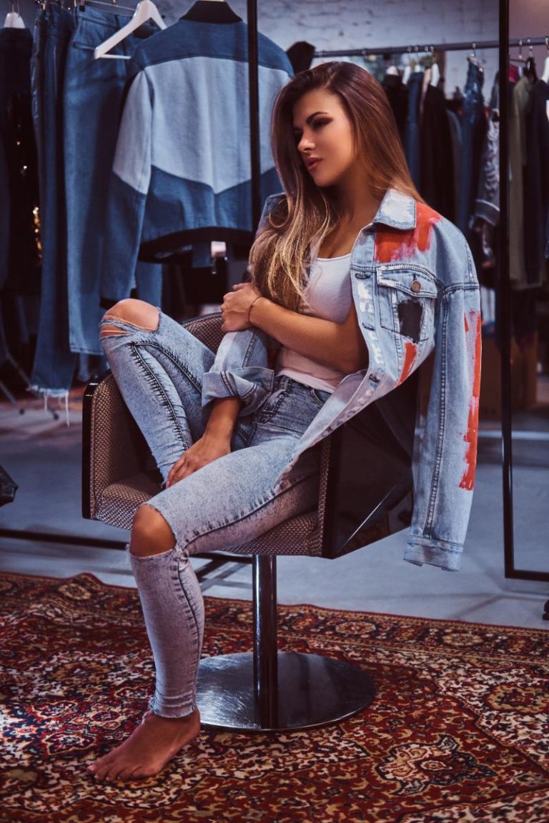 stylish-girl-wearing-distressed-jeans-coat-covering-his-shoulder-sitting-chair-fitting-room-clothing-store